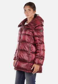 Cappotto imbottito borgogna con collo alto, chiusura frontale con zip, tasche laterali e polsini elasticizzati. Materiale liscio e lucido con motivo trapuntato.