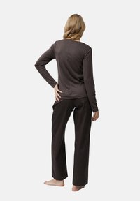 Braunes Longsleeve-Oberteil kombiniert mit dunklen, gestreiften Hosen. Das Outfit hat eine lockere Passform, glattes Material und keine sichtbaren Hardware-Elemente oder Muster.