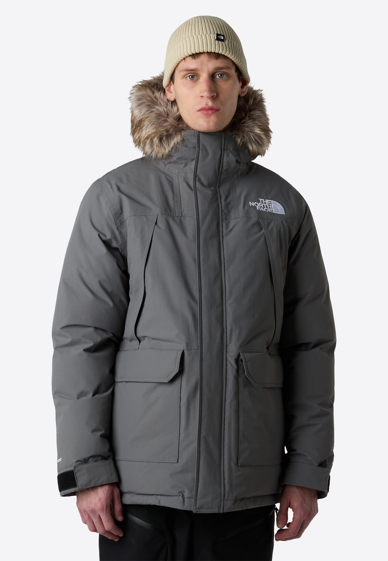 Grå isolerad jacka med avtagbar huva i päls, två framfickor och justerbara manschetter. Enkelt design, väderbeständigt material.