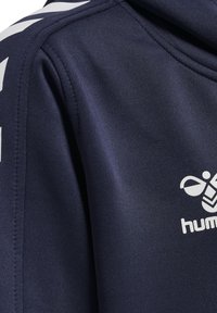 Felpa sportiva navy realizzata in tessuto morbido e testurizzato. Presenta strisce diagonali bianche sulla spalla e un logo stampato sul petto.