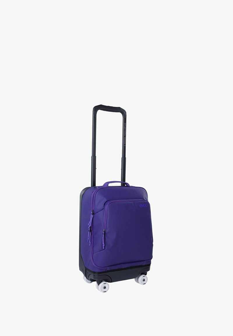 Maleta morada con ruedas, exterior de tela, dos bolsillos frontales y un asa retráctil. Cuenta con cuatro ruedas blancas para facilitar el desplazamiento.