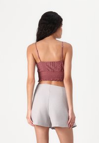 Heklet topp i støvet rosa med spaghetti-stropper og smock-detaler, kombinert med høyt liv grå shorts med en glatt tekstur.