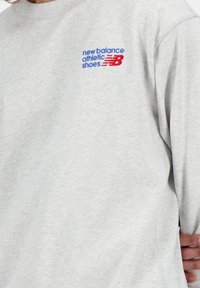 Sweatshirt gris en mélange de coton doux, avec un logo brodé bleu et rouge sur la poitrine gauche, doté d'une coupe décontractée et d'un col rond.