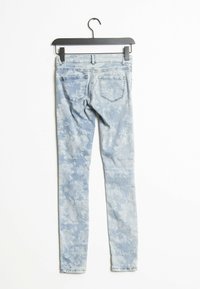 Floral print light blue jeans hanging on a black hanger, featuring five-pocket design and tapered leg with a faded texture.