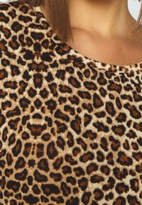 Látka s leopardím vzorem, s béžovým pozadím a černými a hnědými skvrnami, s ribbovanou texturou a kulatým výstřihem.