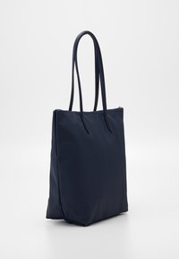 Marinblå totebag i strukturerat material med långa handtag, rektangulär form och dragkedjestängning upptill. Enkel och funktionell design.