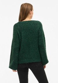 Maglione verde a maglia con una vestibilità ampia, spalle cadenti e maniche larghe. Tessuto texturizzato con un aspetto morbido e caldo.