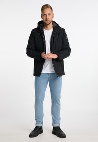 Schwarze Kapuzenjacke mit Reißverschluss, grauem Innenfutter und seitlichen Taschen. Hellblaue Jeans und schwarze Sneakers runden das Outfit ab.
