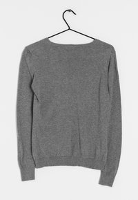 Pull gris à manches longues en tricot suspendu à un cintre noir sur un fond blanc uni, vu de dos.