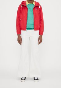 Czerwona lekka kurtka, zielony sweter, białe rozszerzane spodnie, czarno-białe trampki. Posiada kaptur i kontrastowy kołnierz.