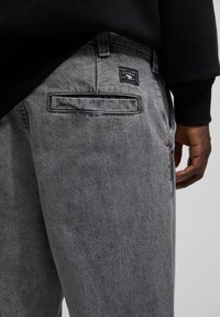 Grå denimbyxor med en bakficka som har en etikett. Tyget har en slät struktur och en lätt sliten look. Avslappnad passform.