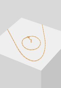 Guldfarvet smykkesæt bestående af en snoet kædehalssmykke og armbånd, begge med en muslingeklipslås og detaljeret udsmykning.