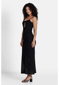 Schwarzes, tailliertes Maxikleid mit Spaghettiträgern, strukturiertem Stoff und einem Schlüssellochdetail an der Brust. Kombiniert mit schwarzen Riemchenheels.