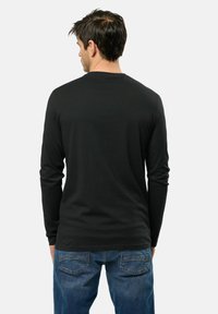 Chemise noire à manches longues avec un col rond, silhouette ajustée et texture lisse, associée à un jean bleu avec des poches arrière.