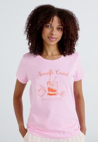 T-shirt de algodão rosa claro com uma impressão laranja de um copo de cocktail com elementos cítricos e o texto "Amalfi Coast Endless Summer."