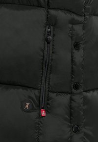 Zwarte pufferjack met een quilted ontwerp. Beschikt over een ritszak, ronde zwarte knopen en een kleine logo patch in rood en grijs.