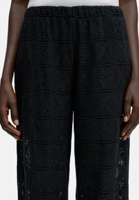 Zwarte gebreide broek met een textuurdesign en opengewerkte accenten, een elastische tailleband en een relaxte pasvorm.