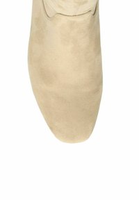 Beige suède schoen met een vierkante neus en zichtbare stiksels bij de opening, getoond vanuit de bovenaanzicht op een witte achtergrond.