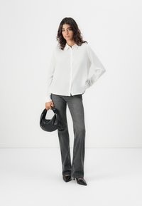 Camicia bianca attillata abbinata a jeans grigi a zampa d'elefante. Borsa nera di forma rotonda. Tessuto morbido, design minimalista.