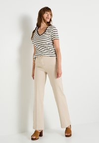 Top de manga corta a rayas en crema y negro, combinado con pantalones de pierna ancha beige y sandalias de plataforma marrones, sobre un fondo blanco.
