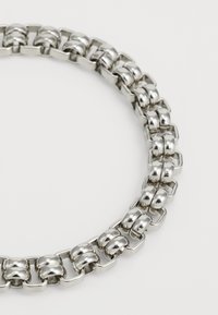 Collier en métal argenté composé de maillons ronds et rectangulaires avec une finition polie, créant une surface texturée et réfléchissante.