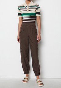 Kurzärmliges Poloshirt mit horizontalen Streifen in Grün, Braun und Creme, kombiniert mit braunen Cargo-Hosen mit elastischen Bündchen und Fronttaschen.