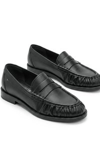 Ζευγάρι μαύρα δερμάτινα penny loafers με στρογγυλεμένο, μαζεμένο σχέδιο στο δάκτυλο και χαμηλό στρωματοποιημένο τακούνι σε λευκό φόντο.