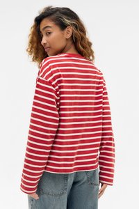 Langärmliges T-Shirt mit roten und weißen Streifen, lockerer Passform und rundem Ausschnitt, aus weichem Stoff. Tragen mit hellblauen Denim-Hosen.