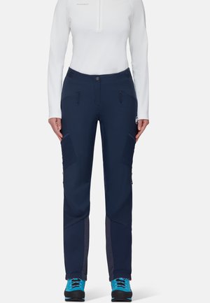Marineblauwe outdoorbroek met meerdere ritszakken, verstevigde accenten en rekbare stof. Gecombineerd met een witte lange mouwtop.