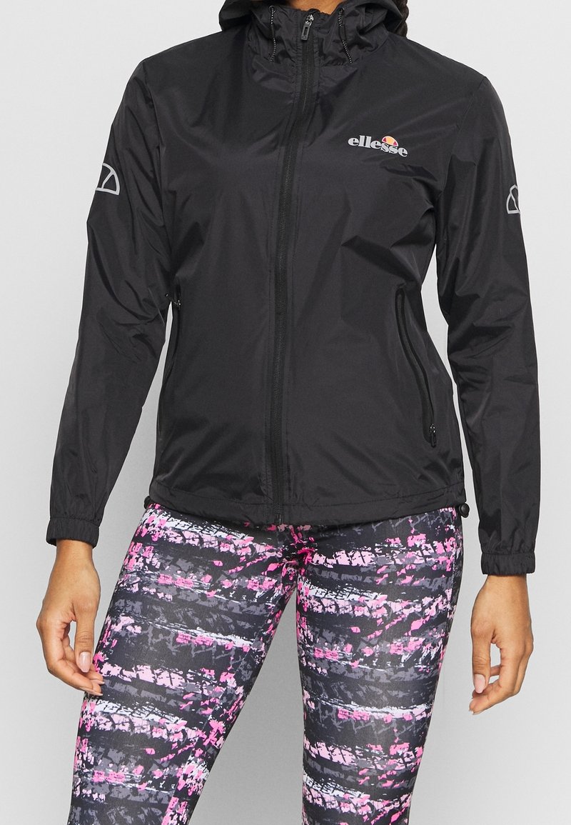 Svart lättviktsjacka med dragkedja framtill, justerbar huva och elastiska muddar. Matchas med mönstrade leggings med rosa och grå ränder.