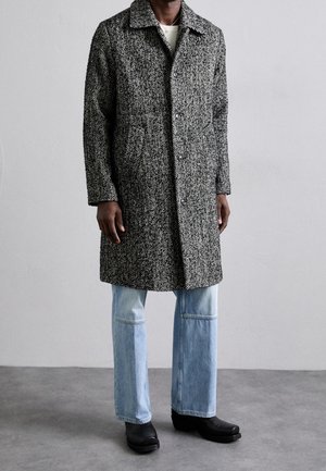 Waarschijnlijk geruit wollen mantel in zwart-wit, met een kraag, zijzakken en een rechte snit, gecombineerd met lichtgewassen, wijde jeans.