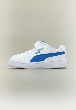 Baskets blanches Puma avec bande latérale bleue, bride auto-agrippante et semelle blanche, présentées sur un fond gris clair.