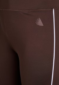 Brown athletic leggings featuring a smooth texture, a slim fit, and a vertical white stripe, with a subtle patterned logo detail.