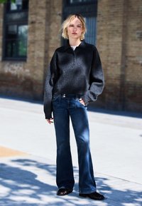 Crni skraćeni pulover s visokim ovratnikom, uparen s tamnoplavim flare trapericama. Outfit se odlikuje minimalističkim dizajnom i mekim materijalom.