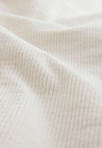 Tessuto bianco rigato con una texture morbida, che mostra sottili linee verticali e una superficie leggermente pelosa. Ideale per l'imbottitura o i tessuti.