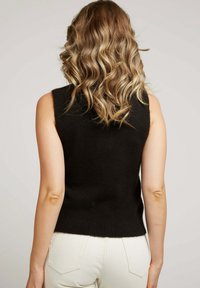 Débardeur noir en tricot sans manches avec une coupe ajustée et un ourlet côtelé, associé à un jean de couleur claire. La vue arrière met en avant la texture et la coupe.