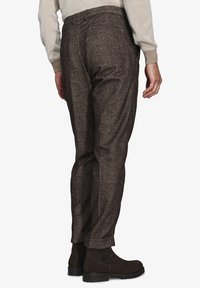 Brune, teksturerede bukser med en tapered design, der har en rullet manchet og baglommer. Bæres med mørke, knælange støvler i ruskind.