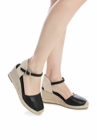 Sandalias de cuña negras perforadas con correas para el tobillo a rayas beige y suelas envueltas en yute. Diseño de espalda abierta para mayor transpirabilidad y comodidad.