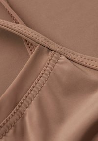 Light brown, smooth fabric featuring a cross-stitch design along the edges and a partially elasticated seam, highlighting its seamless construction.