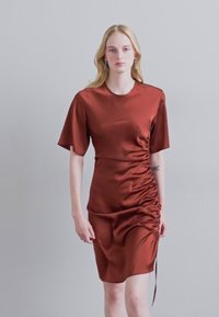 Satinová šaty v rustikálnej farbe s krátkymi rukávmi a bočným riasením. Majú zaoblený výstrih a bočný detail viazania.