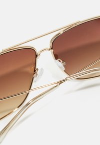 Gafas de sol doradas con lentes degradados marrones, que presentan una elegante forma rectangular, almohadillas para la nariz y delgadas varillas de metal.