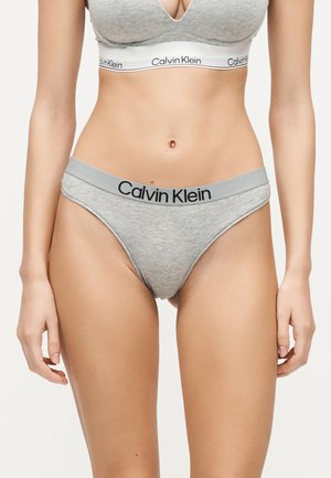 Femme portant un ensemble soutien-gorge et sous-vêtements gris clair Calvin Klein assorti avec des bandes élastiques marquées, montré de la poitrine jusqu'aux cuisses.