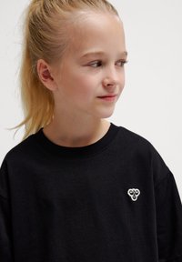Sort bomulds T-shirt med korte ærmer, prydet med et lille hvidt broderet logo på brystet. Glat tekstur, afslappet pasform.
