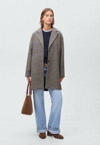 kariran plašč v rjavih in modrih tonih, dolgi rokavi, velik ovratnik, z gumbi, kombiniran s svetlimi kavbojkami ter rjavo torbico in čevlji.