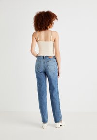 Lichtblauwe high-waisted jeans met een rechte pijp en subtiele vervaging, gecombineerd met een beige tanktop en witte block-heeled schoenen.