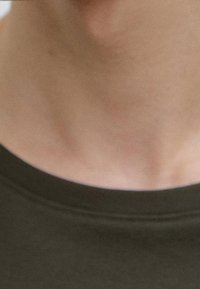 Ciemnozielona bawełniana koszulka typu crew neck o gładkiej teksturze, ukazująca dekolt i gładką skórę szyi poniżej.