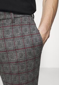 Pantalons gris à carreaux en tissu texturé, présentant un motif de grille rouge subtil, avec une taille plate et des poches latérales.