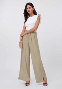Hvit ribbet topp med volanger på ermene, kombinert med brede beige bukser med frontslisser. Svarte sandaletter med stropper fullfører antrekket.