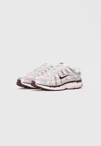 Nike tenisice s ružičasto-srebrnim dizajnom, mrežastim gornjim dijelom, teksturiranim detaljima i čvrstim burgundskim potplatom.