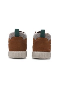 Par de zapatillas de ante marrón con cuello de tela gris en el tobillo, tiradores verdes y suelas blancas texturizadas mostradas desde la parte trasera.